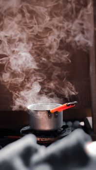 A metal saucepan with steam rising, placed on a stove with a red handle.