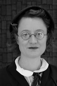 Black and white portrait of a woman in 1940s attire with vintage round glasses.