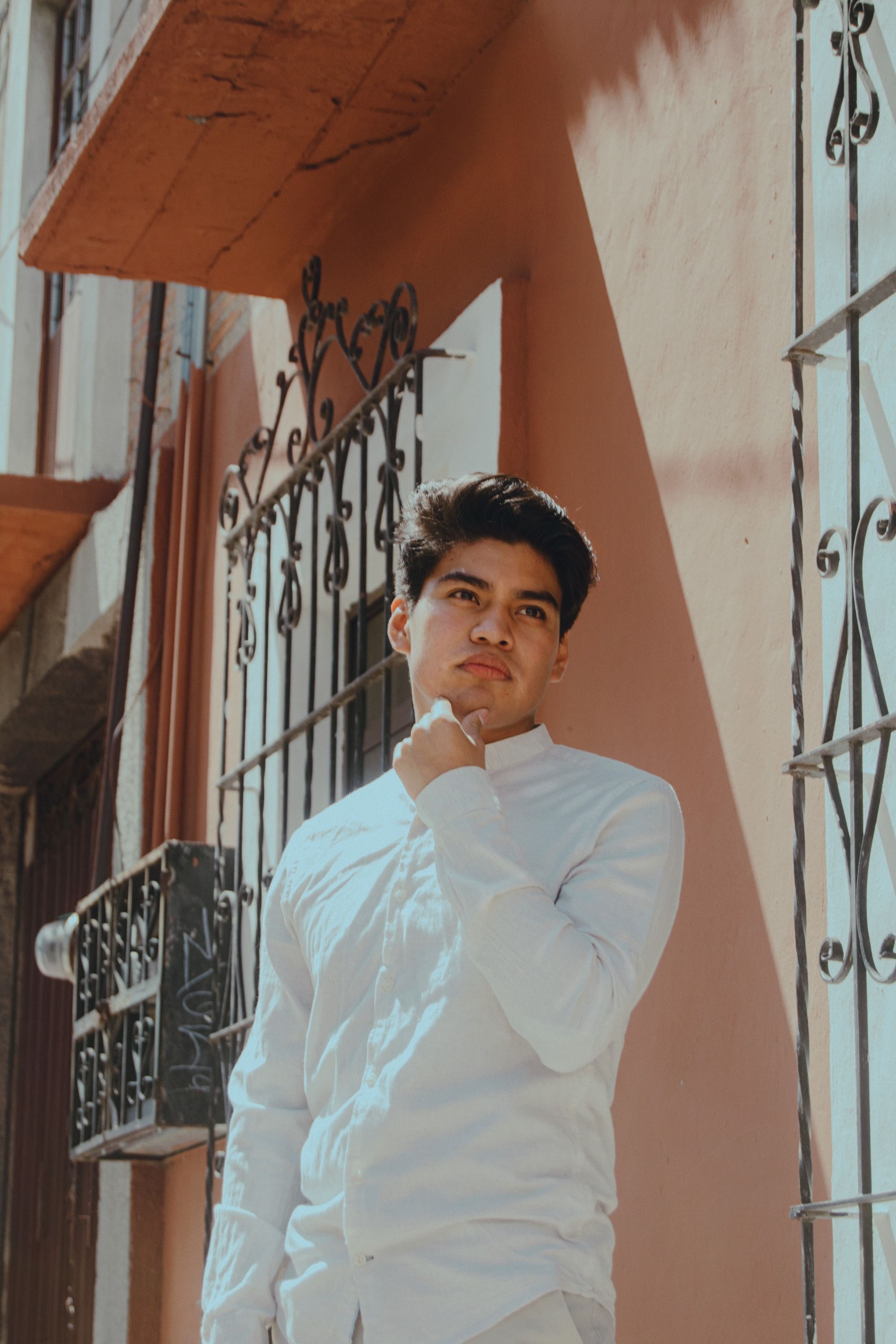 Young man in white shirt posing thoughtfully in sunny urban environment.