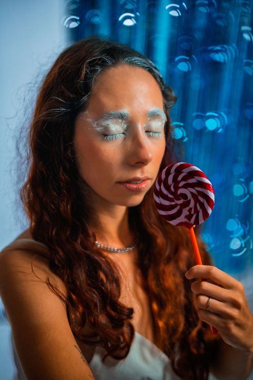 Free Artistic portrait of a woman with whimsical makeup holding a candy lollipop. Stock Photo