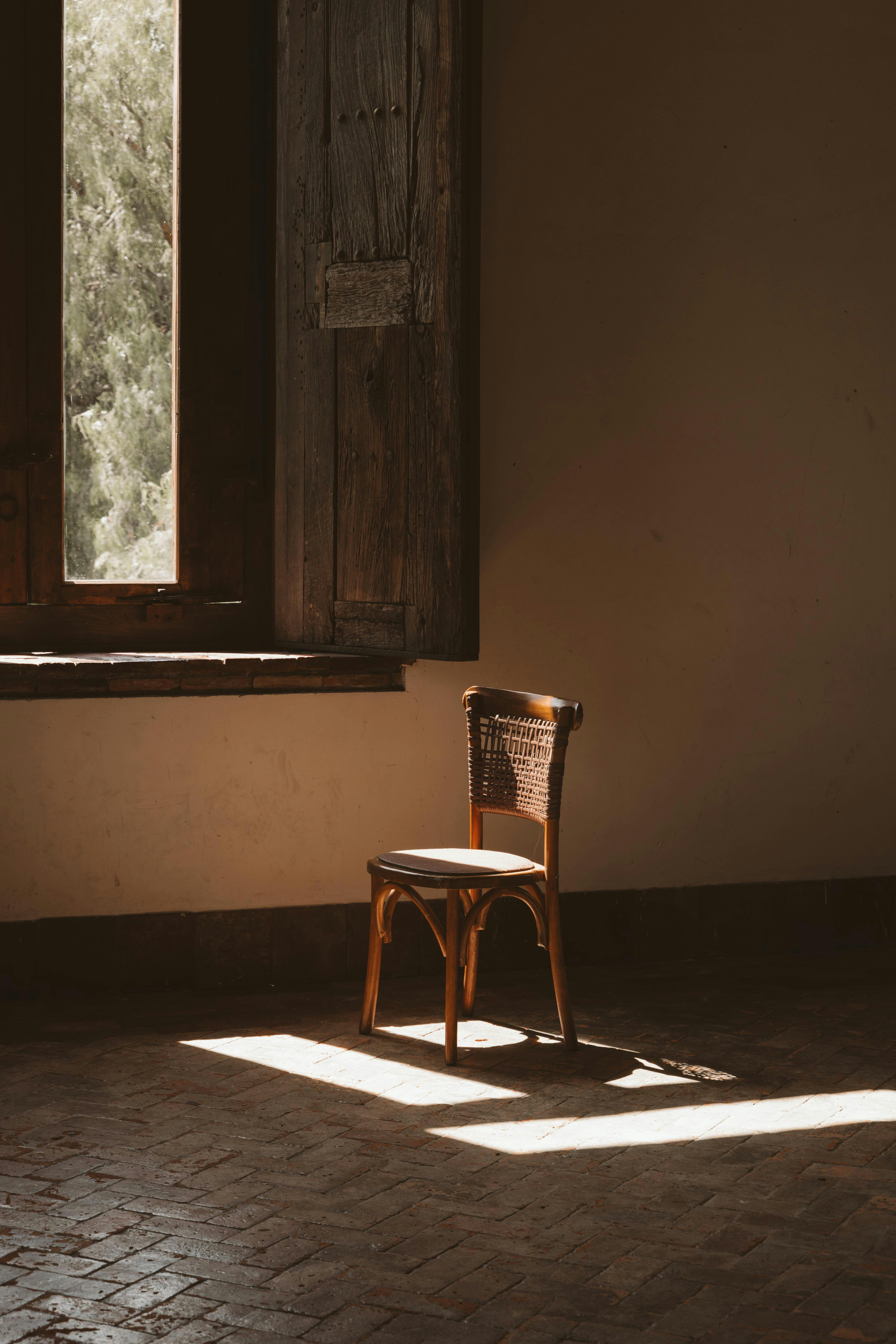 A rustic wooden chair bathed in sunlight by an old wooden window, creating a serene atmosphere.