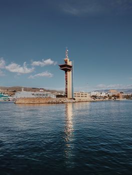 Tall coastal tower reflecting in calm waters under a clear sky.
