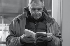 Senior man in a jacket reads a book indoors in a calm setting.