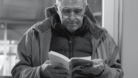 Senior man in a jacket reads a book indoors in a calm setting.