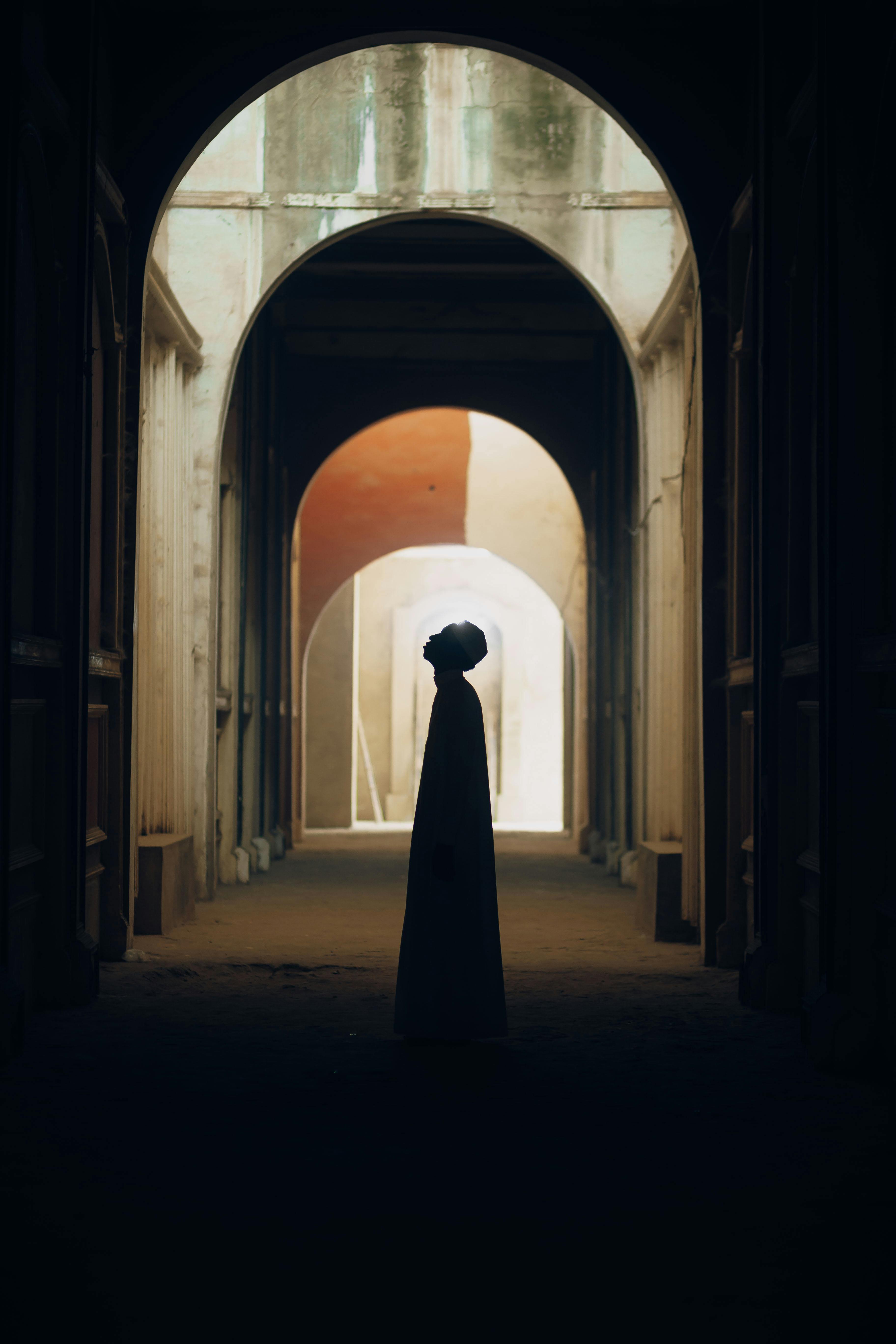 A silhouette stands in a mystical corridor with arches, creating a dramatic atmosphere.