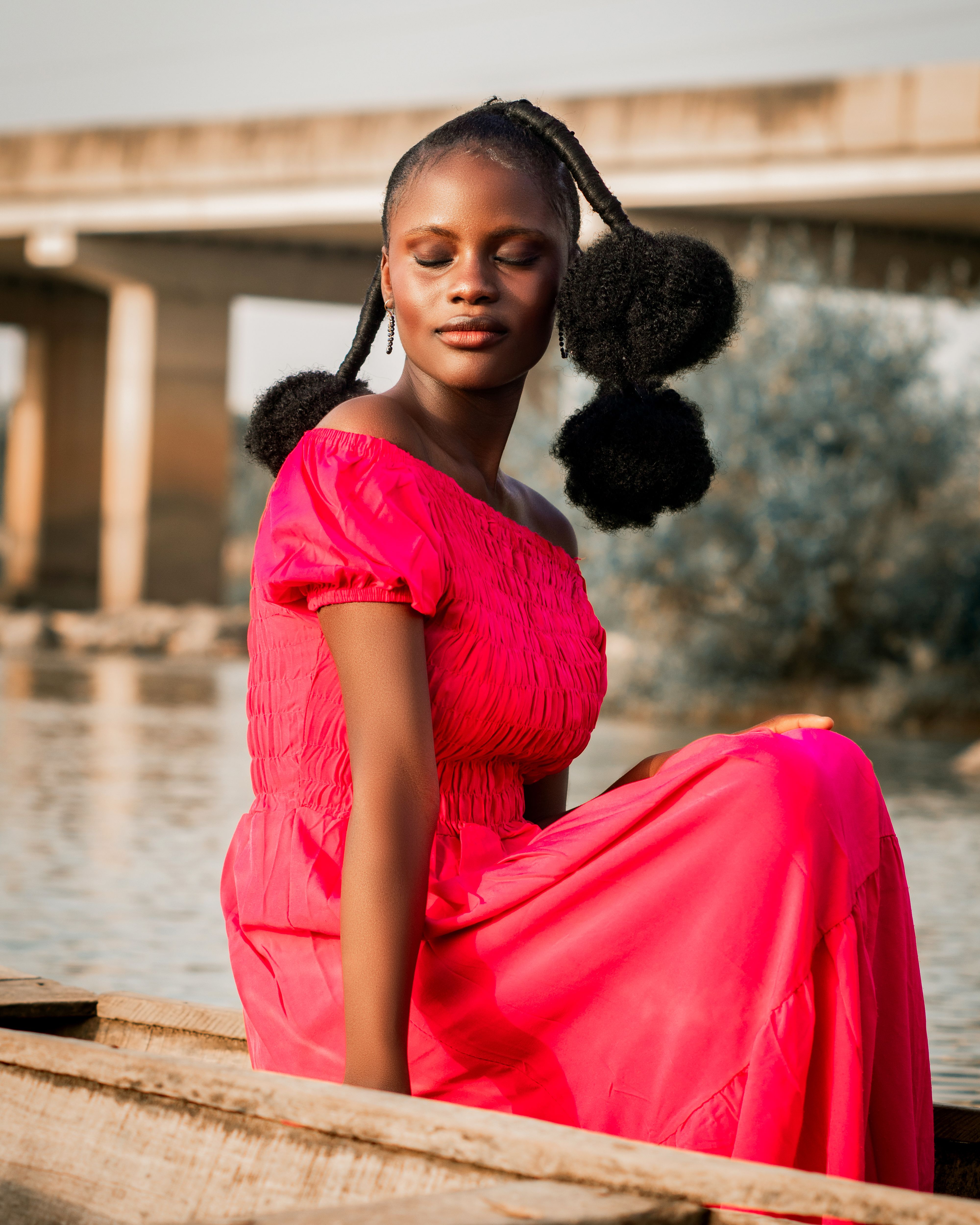 A woman in a pink dress sitting serenely by the riverside, exuding calmness and beauty.