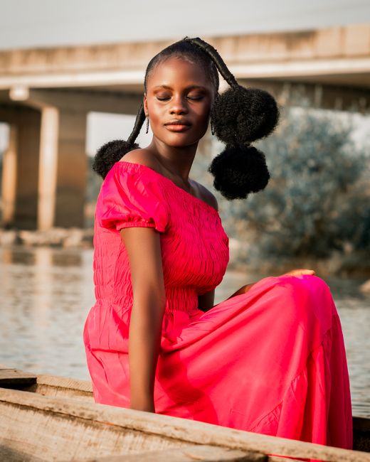 A woman in a pink dress sitting serenely by the riverside, exuding calmness and beauty.