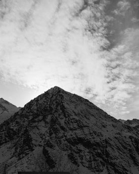 Black and white photo of a snowcapped mountain with dramatic clouds overhead.