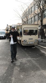 Man walking near a food truck on a city street, carrying groceries.