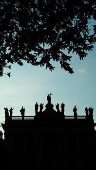 Silhouette of statues atop a historic building with dramatic sky and tree branches, perfect for travel themes.