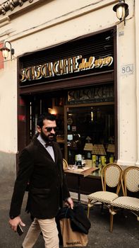 Man with sunglasses walking by a vintage-styled cafe. Urban street view.