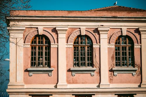 Free Close-up view of a historic building with arched windows and weathered facade, seagull on roof. Stock Photo