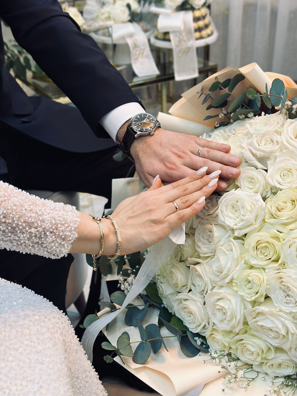Elegant wedding scene with couple's hands on a white rose bouquet, showcasing rings.