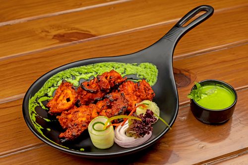 Free Spicy tandoori chicken served on a black plate with green chutney and salad garnishes. Stock Photo