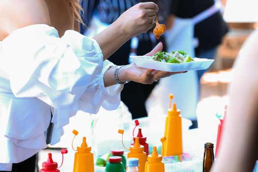 A person outdoors adding sauce to tacos, surrounded by condiment bottles.