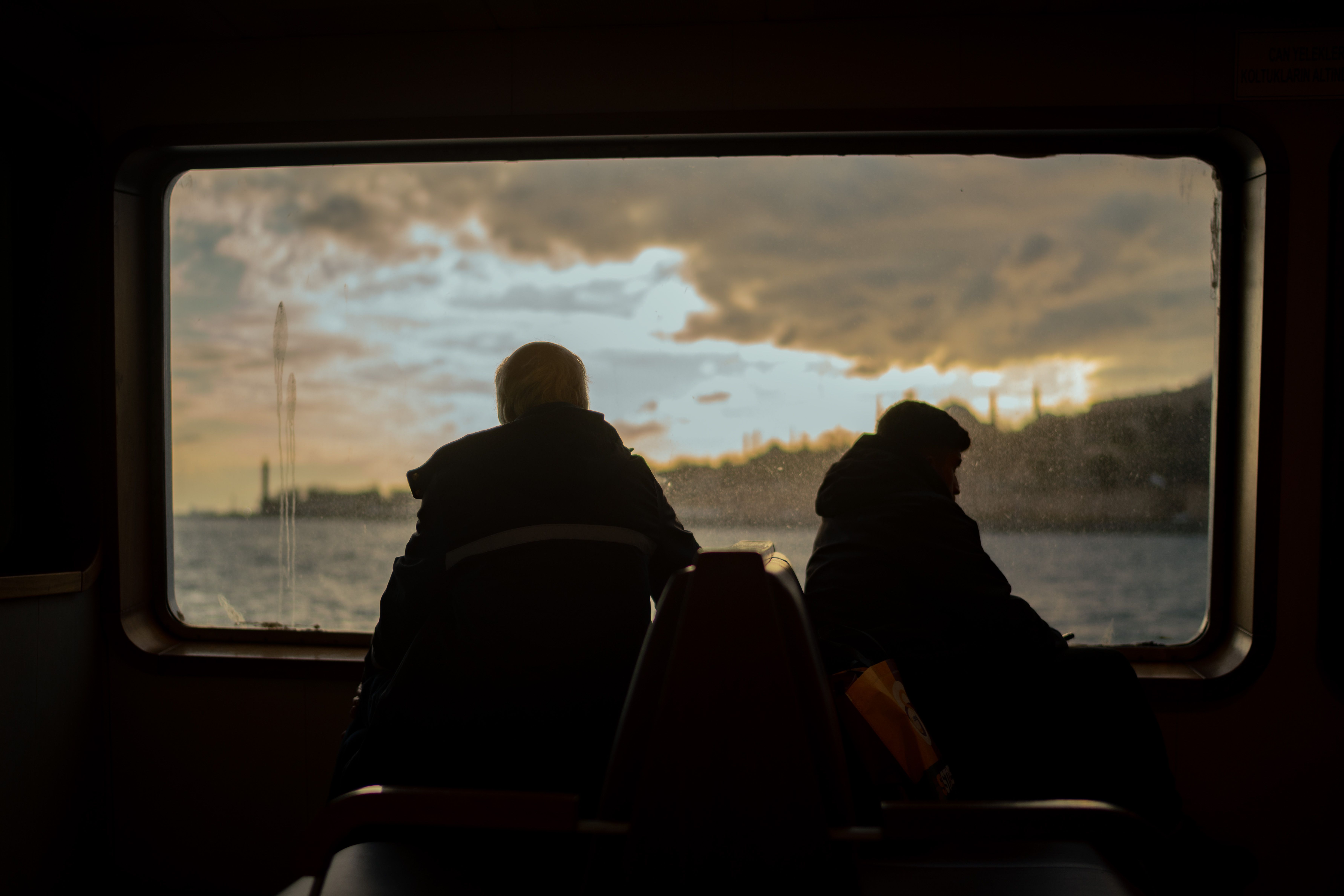 Two silhouettes view the serene sunset from a ferry window, creating a contemplative mood.
