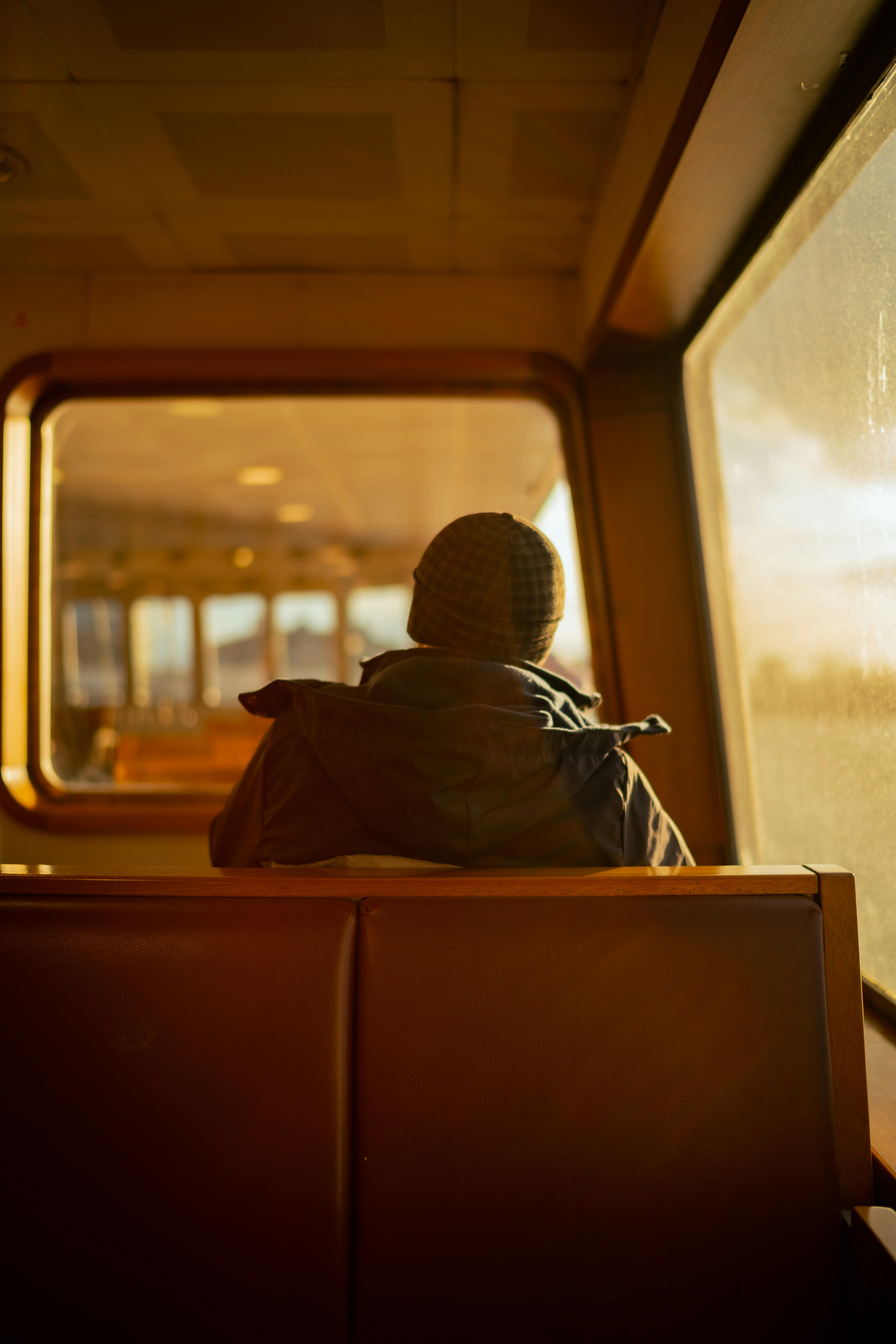 A person in winter attire enjoys a quiet ferry ride with warm light filtering in.