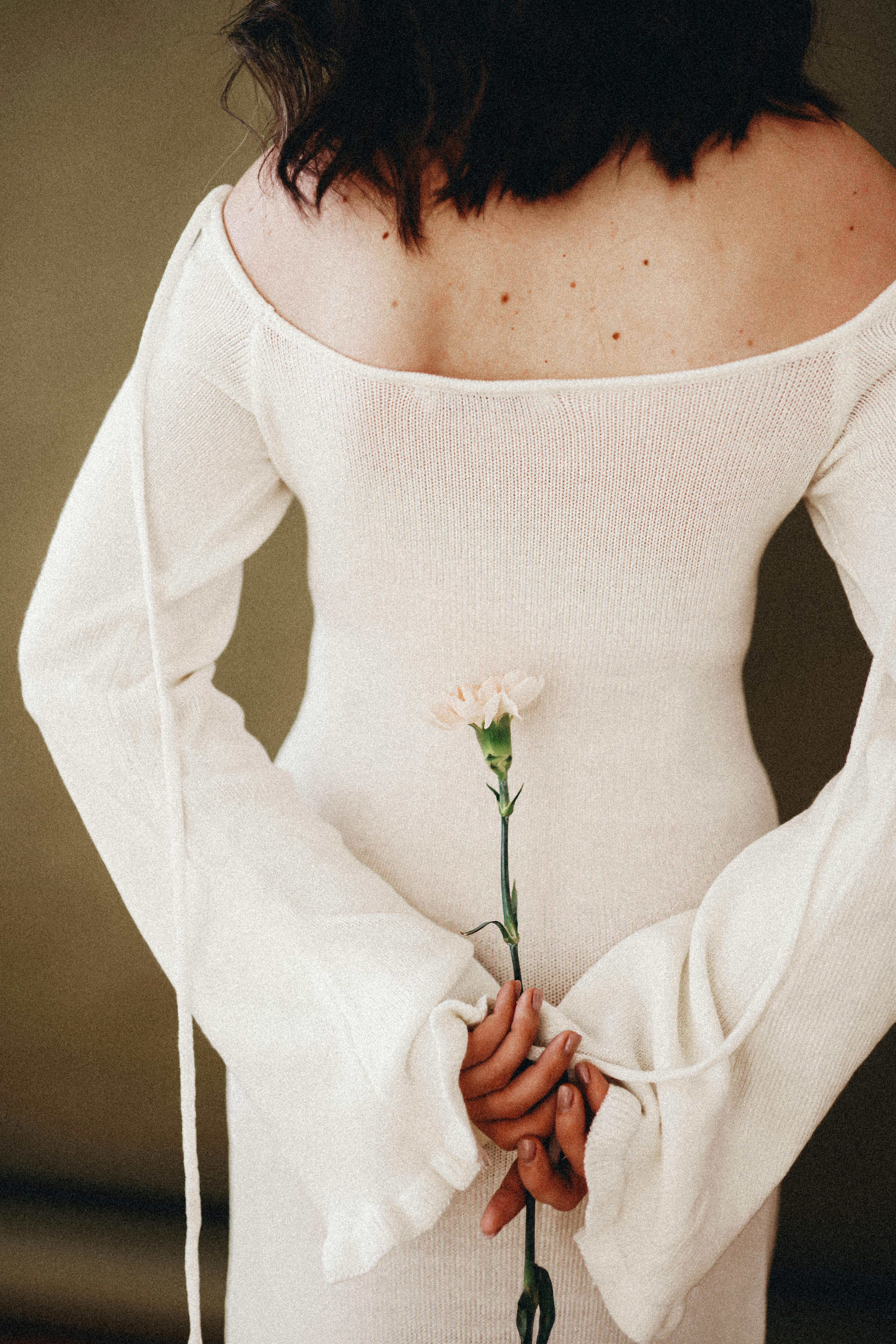 Rear view of a woman in a white dress holding a single carnation flower.