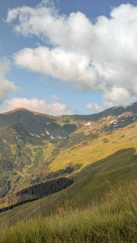 Breathtaking view of a lush green mountainside under a bright blue sky with clouds.