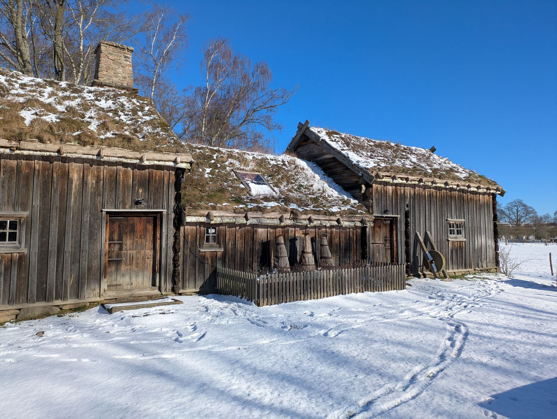 A rustic wooden cabin with moss roof in a snowy winter landscape.
