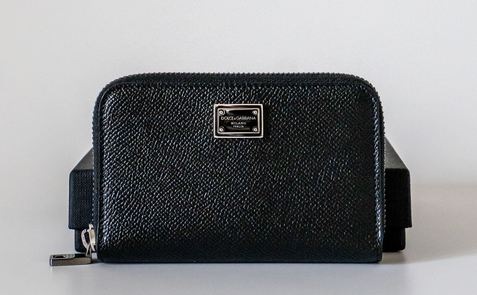 Elegant black leather wallet with metallic logo plate, ideal for fashion enthusiasts.