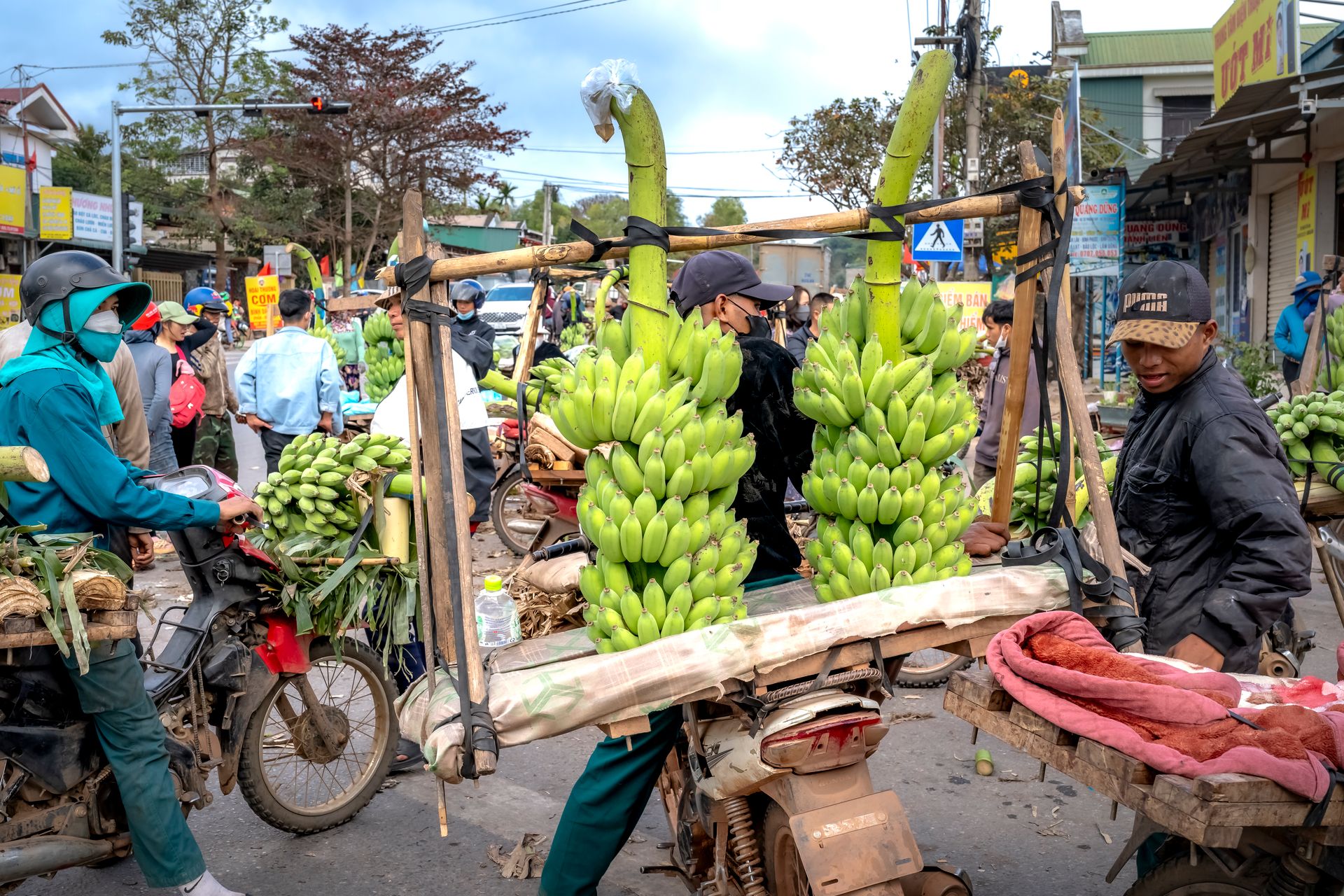 Vibrant outdoor market scene with vendors selling bananas on motorbikes.