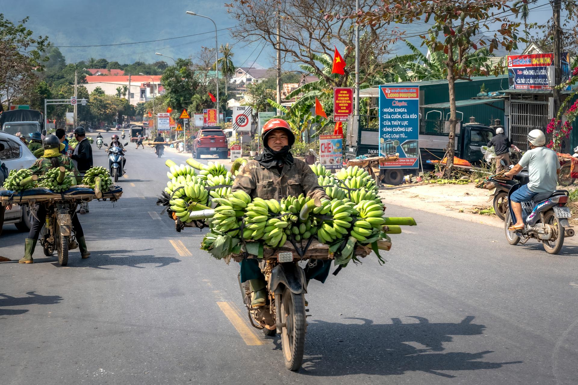 Motorcyclists operate through a busy street in Vietnam, transporting bananas on modified bikes.