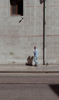 A man walks along a sidewalk beside a textured wall in İstanbul, Türkiye.