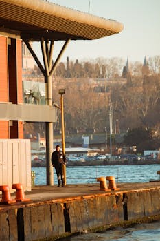 A man stands on a dock in Istanbul at sunset, near the Bosphorus shoreline.