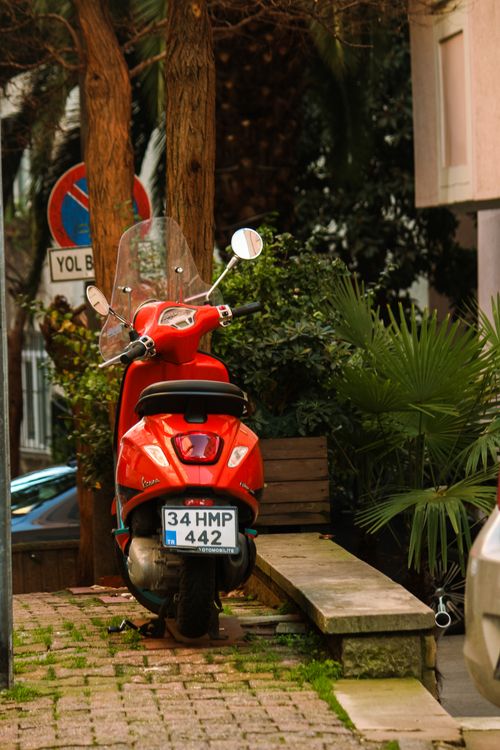 Free A vibrant red scooter parked on a cobblestone street in Istanbul surrounded by greenery. Stock Photo
