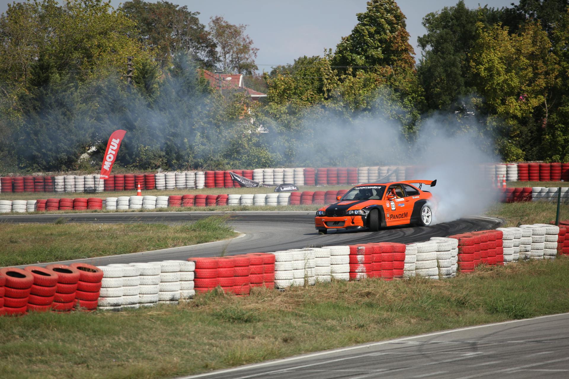 Orange car drifting on a racetrack with smoke and vibrant barriers.