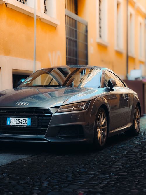 Free Silver sports car parked on a sunlit cobblestone street with European architecture. Stock Photo