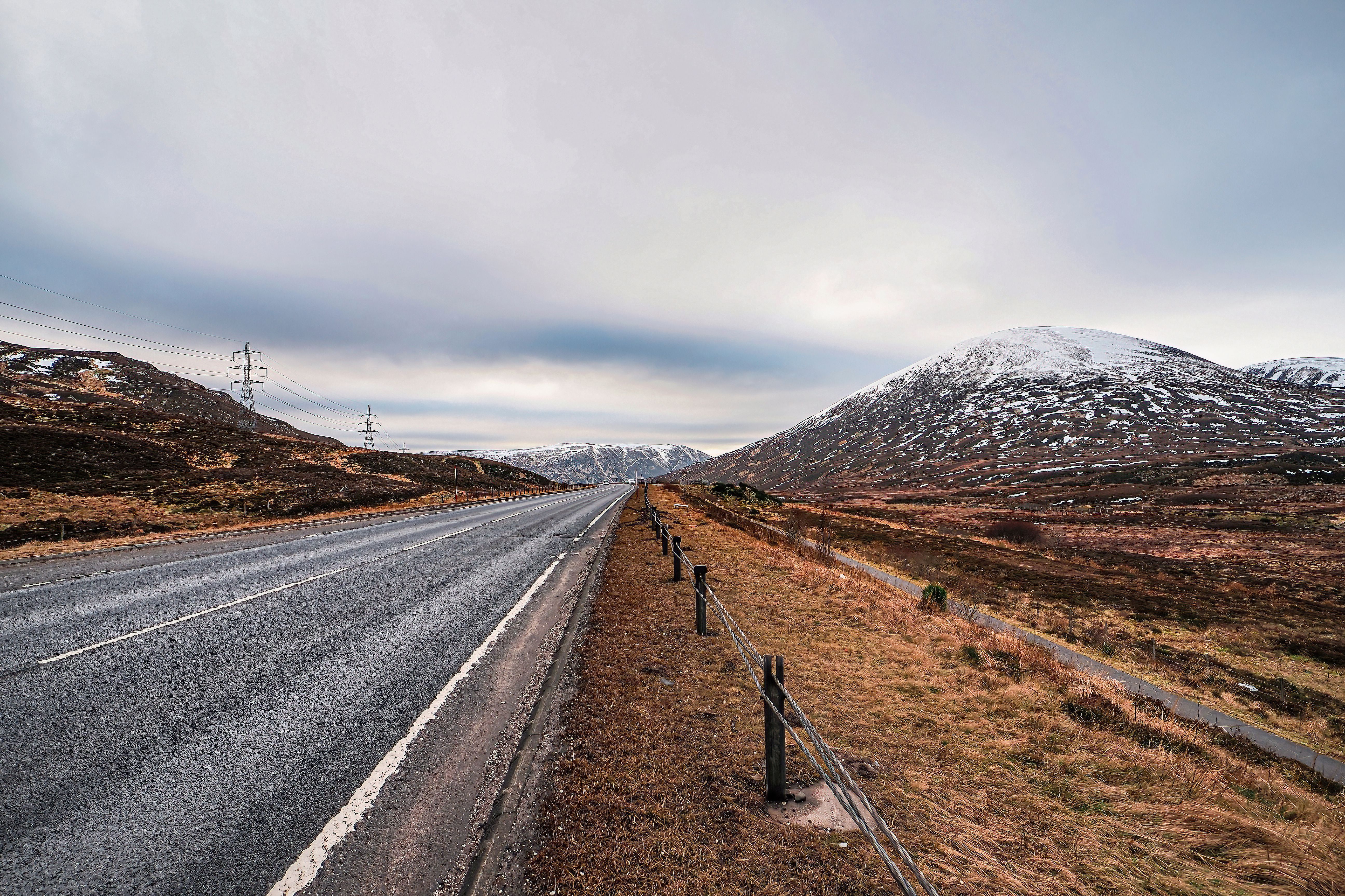 A cleared main road crossing brown winter moor below a snow-capped hill