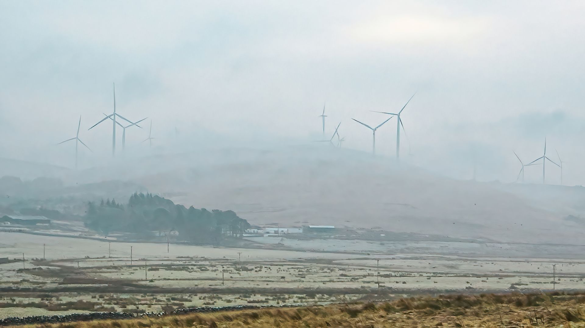Misty landscape with wind turbines on a hill showcasing renewable energy.