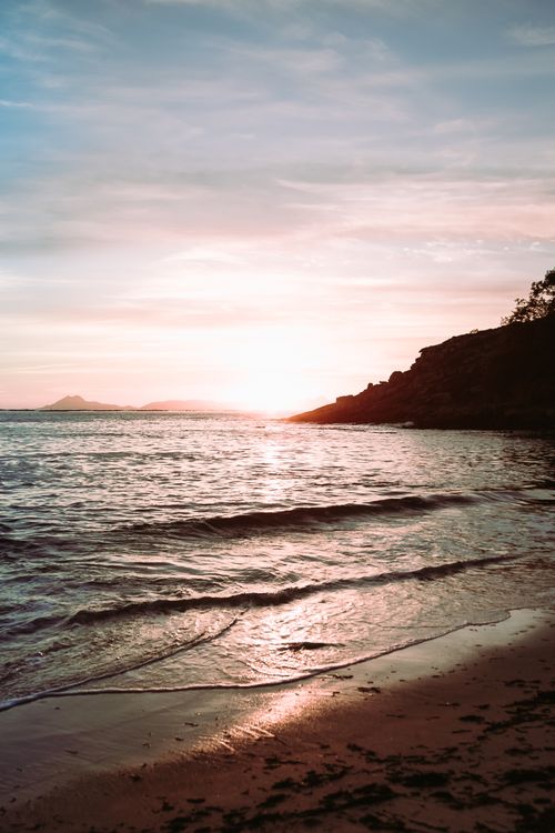 Free Peaceful ocean scene at sunset with waves gently lapping a sandy shore and soft clouds overhead. Stock Photo