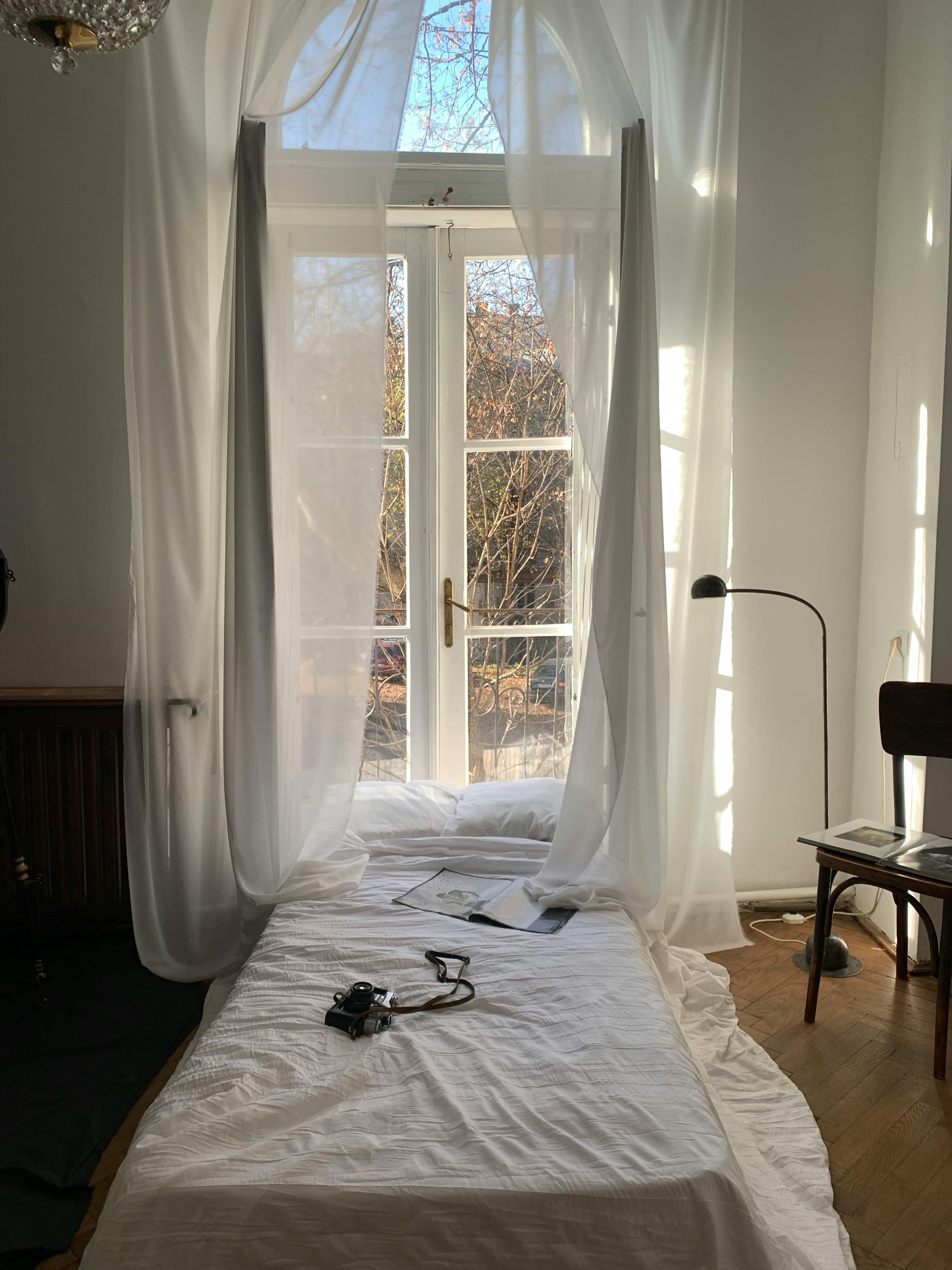 Free Bright minimalist bedroom with white curtains and a camera on the bed. Stock Photo