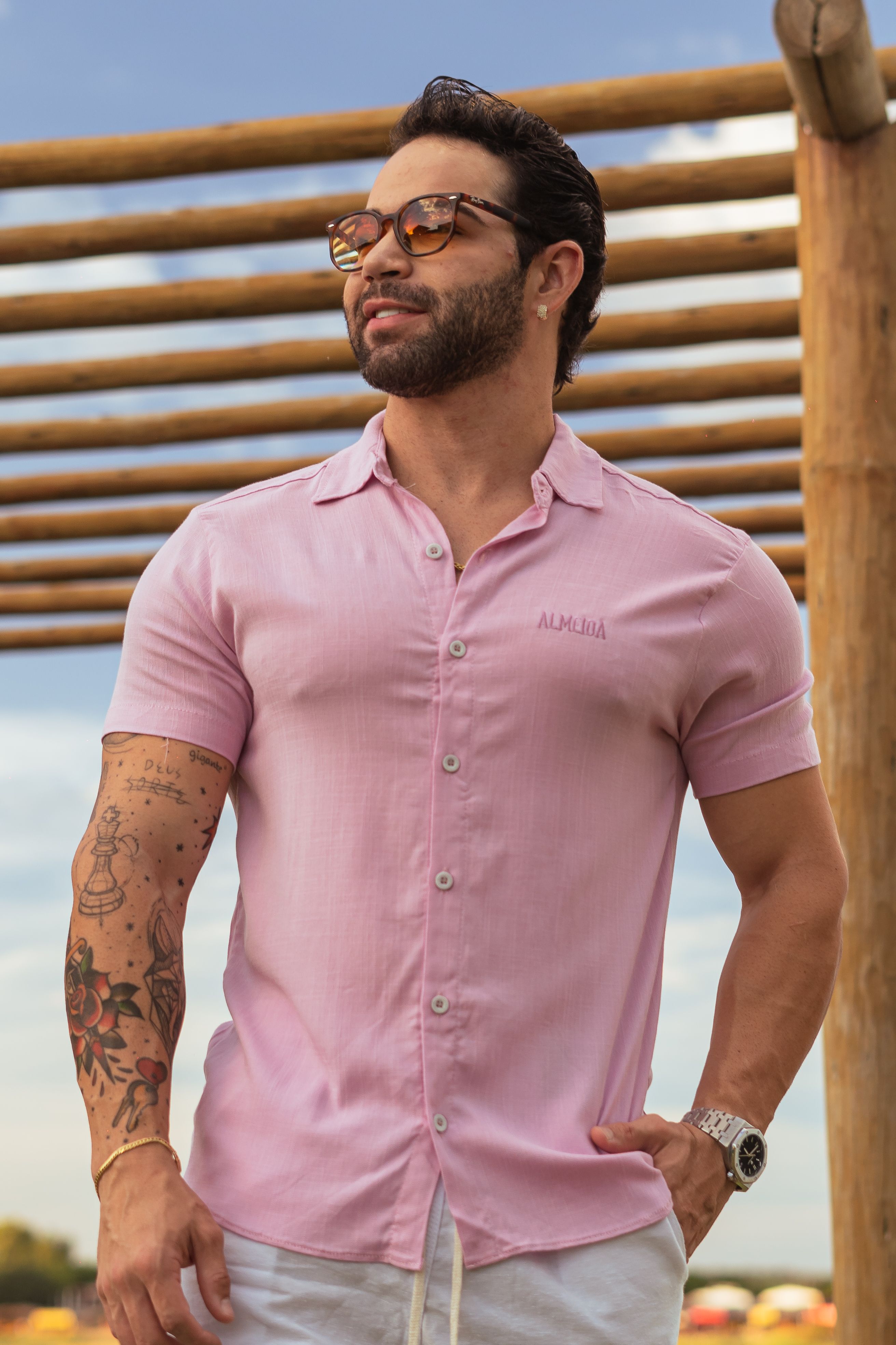 Stylish man wearing sunglasses and a pink shirt outdoors.
