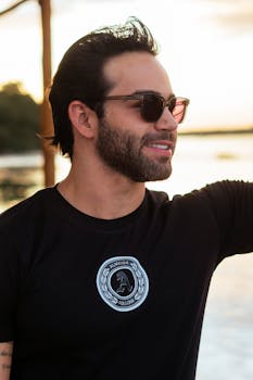 Portrait of a young man wearing sunglasses and a black t-shirt, enjoying the sunset outdoors.