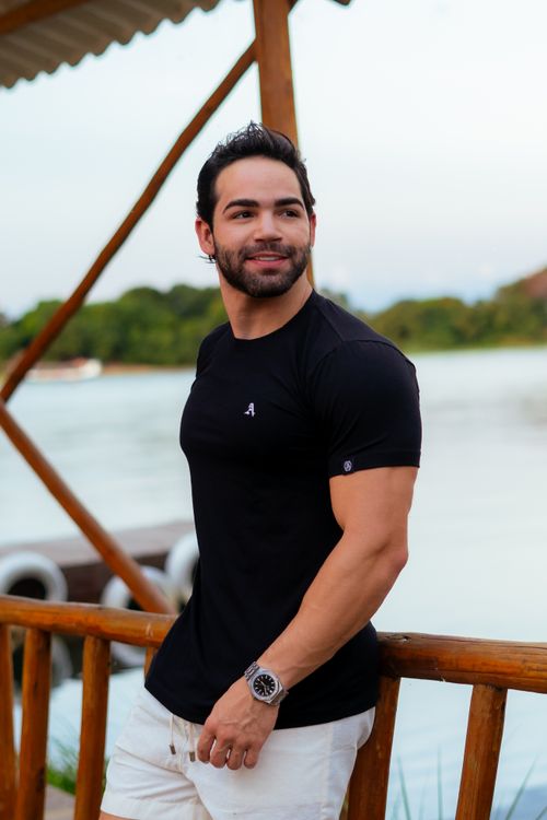 Free Smiling man in a black shirt stands on a wooden deck by a riverside. Stock Photo