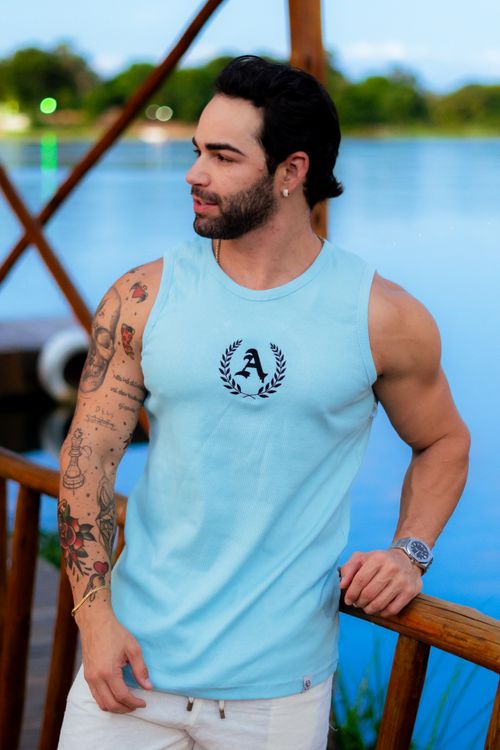 Free Muscular man in a blue tank top with tattoos standing by a lakeside, looking away thoughtfully. Stock Photo