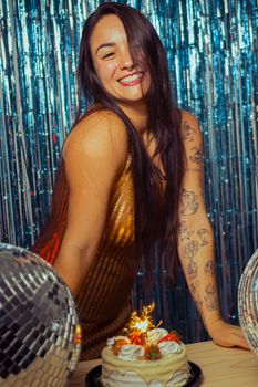 Smiling woman in a festive setting with cake and disco balls, celebrating a special occasion.