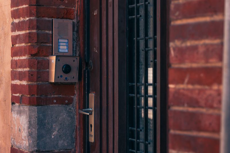 Close-up of a brick wall with a security intercom and door handles in Toulouse, France.