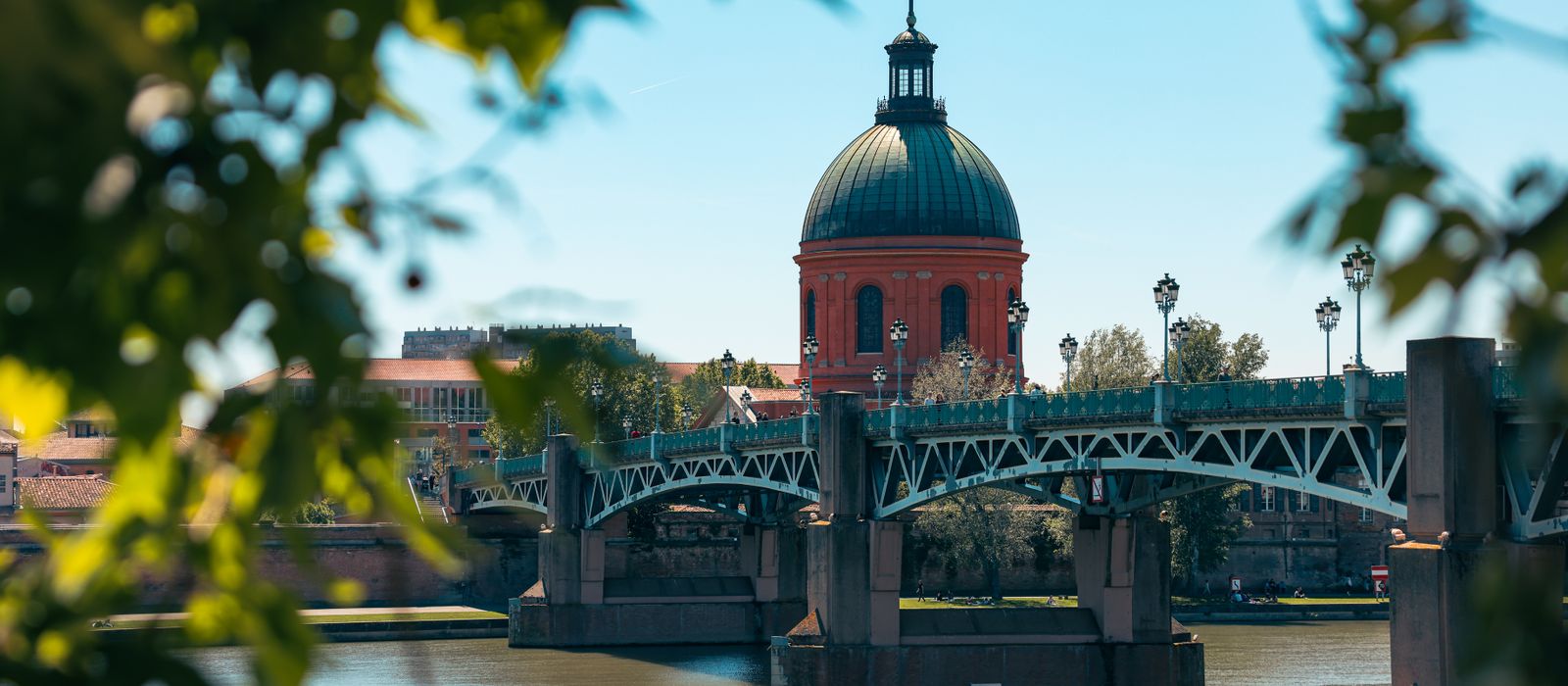 Scenic view of Pont Saint-Pierre and red dome in Toulouse, France framed by leaves. — flights from Strasbourg to Toulouse
