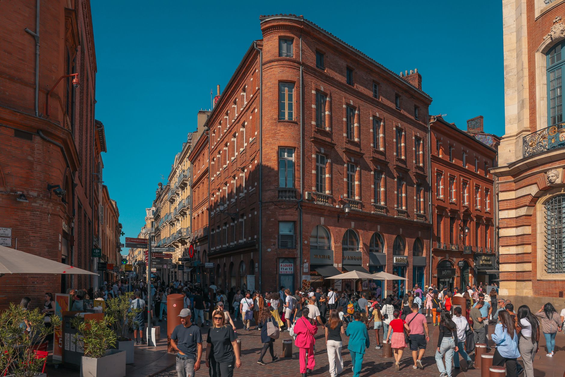 Vibrant street scene in Toulouse's historic district with crowds and red brick architecture.