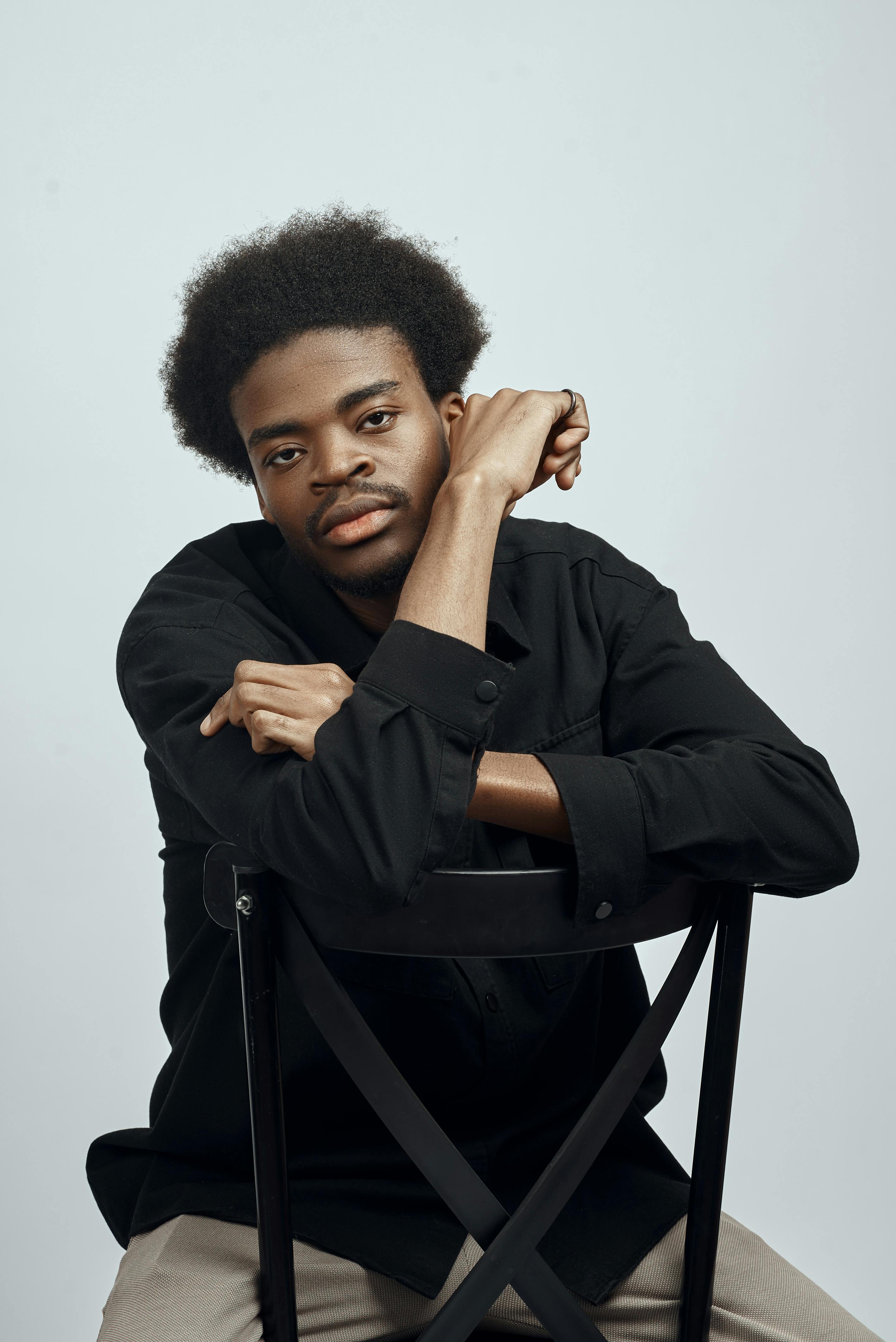 Studio portrait of a young man with afro hair leaning on a chair in İstanbul.