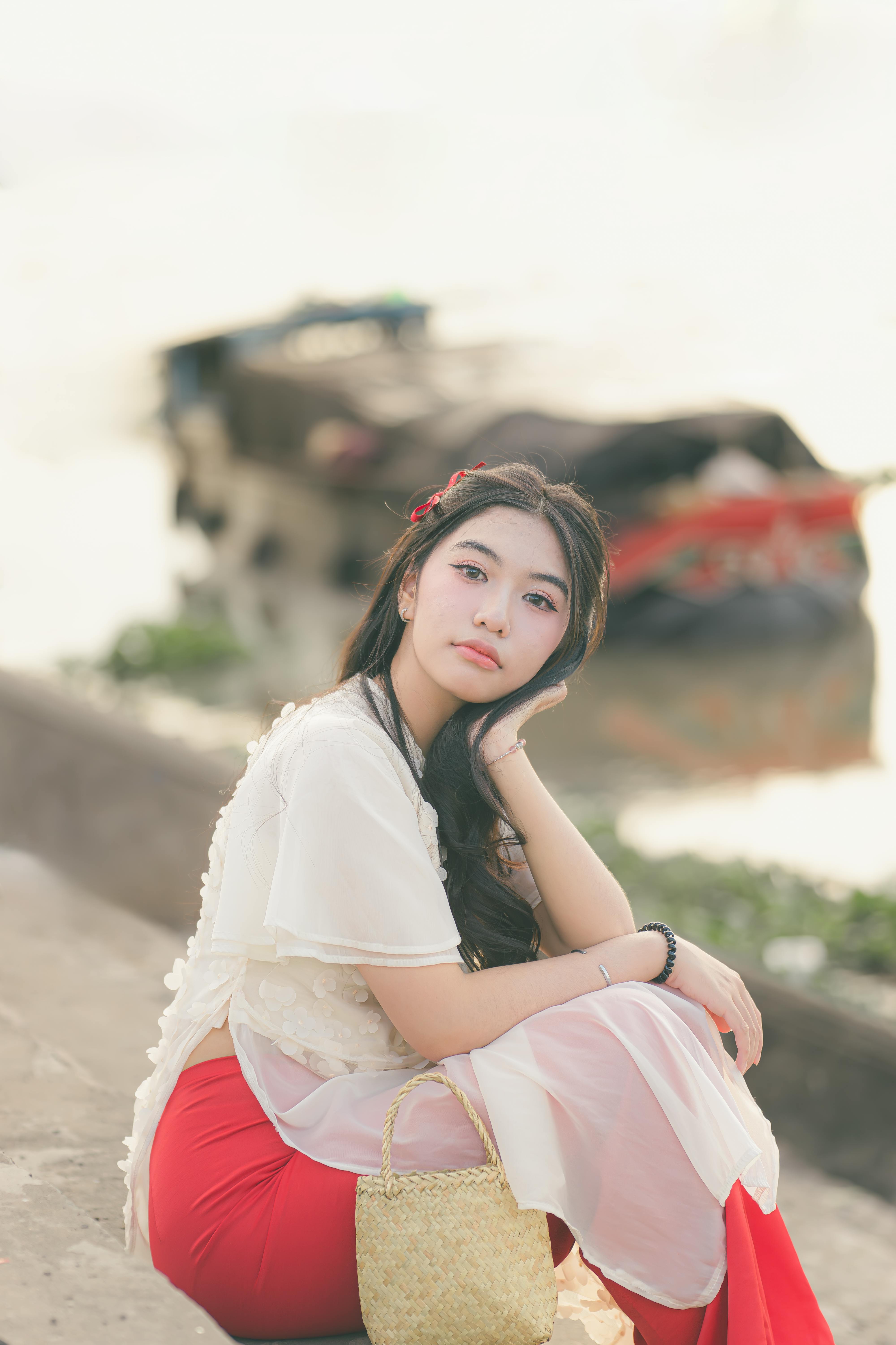 Elegant young woman in traditional attire sitting by a riverside, reflecting serenity and grace.