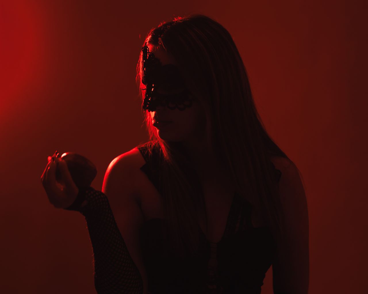 a mysterious woman in a black mask holds an apple under dramatic red l