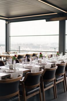 Beautifully arranged dining tables in a modern restaurant with glass walls and city view.