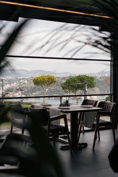 Chic restaurant interior with stunning view of coastal city and lush greenery.
