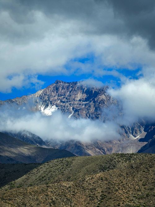 Free Stunning view of a majestic mountain peak enveloped by clouds under a bright blue sky. Stock Photo